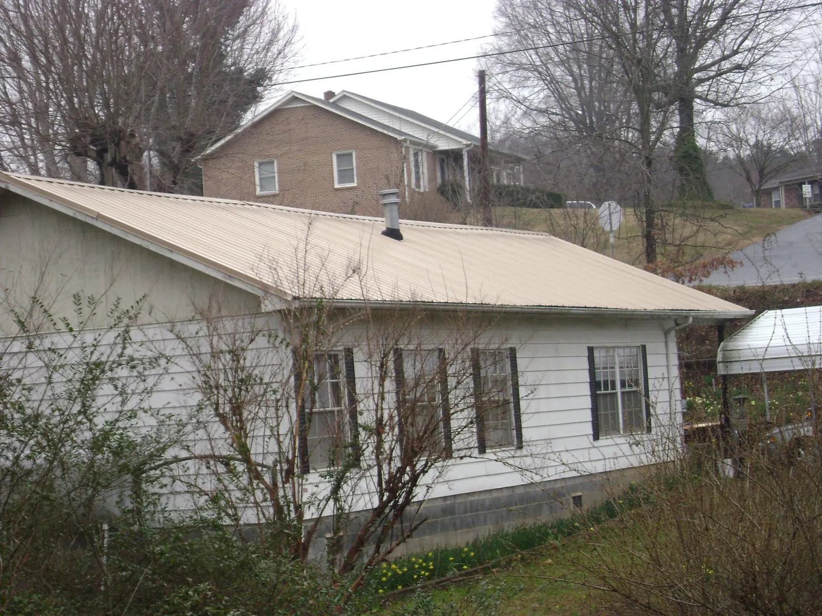 Tan metal roof on a white sided house set into a hillside — Commercial Roofing by Roofing Brothers in Dallesport